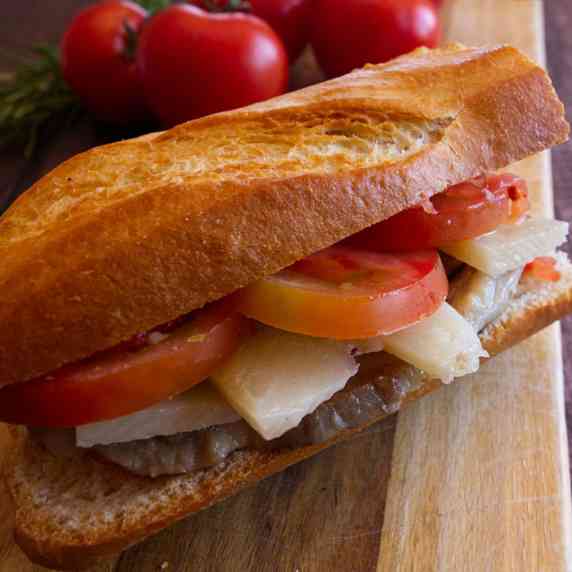 a pork lion sandwich sits with some fresh tomato and cheese
