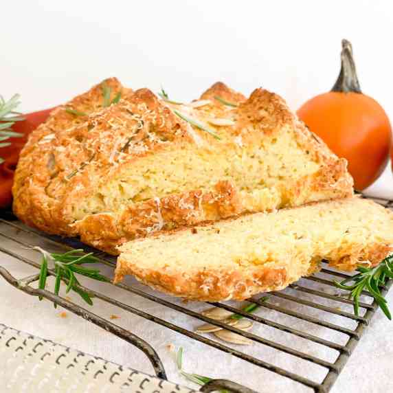 rosemary asiago pumpkin soda bread on a cooling rack with pumpkin seeds, rosemary, and grated asiago