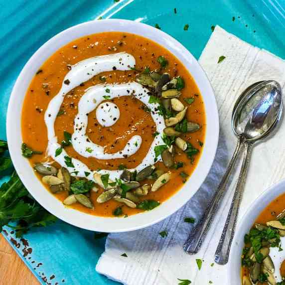 Carrot Pumpkin Soup in a white bowl garnished with coconut milk, parsley, and pepitas.