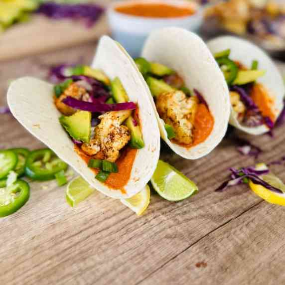Three prepared Roasted Cauliflower Tacos with Romesco Sauce on a wooden table