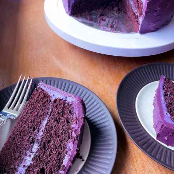 Two slices of purple velvet cake and the cake on a stand