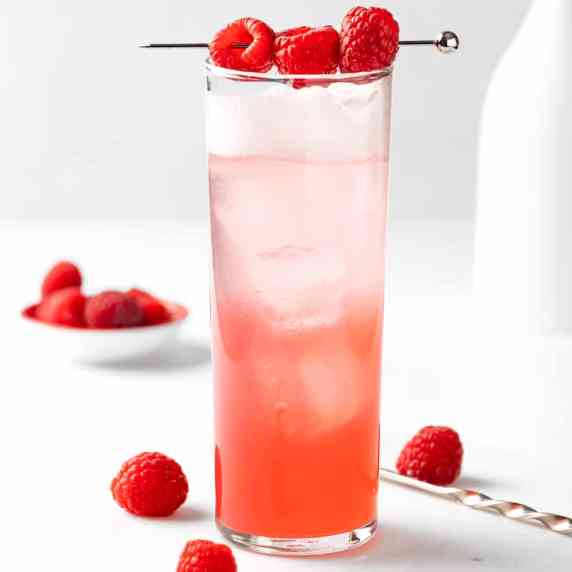 A raspberry gin fizz garnished with fresh raspberries, on a white background. 