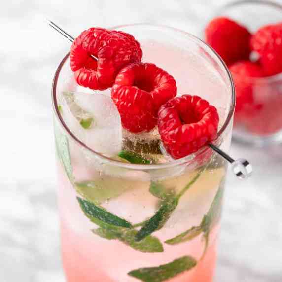 A raspberry mojito mocktail garnished with raspberries and mint leaves