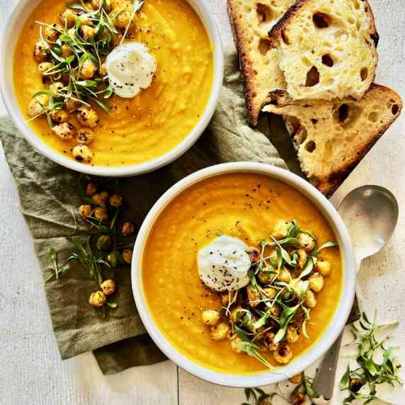 2 white bowls filled with carrot soup topped with yoghurt, chickpeas and microgreens. B