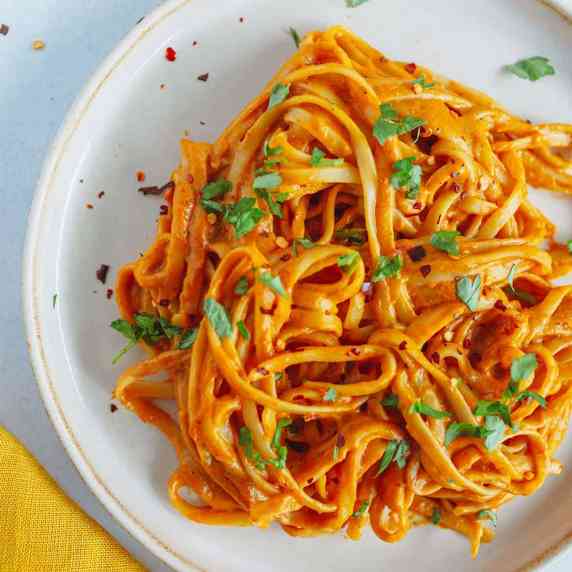 pasta with red pepper sauce on a creamy plate with yellow kitchen cloth