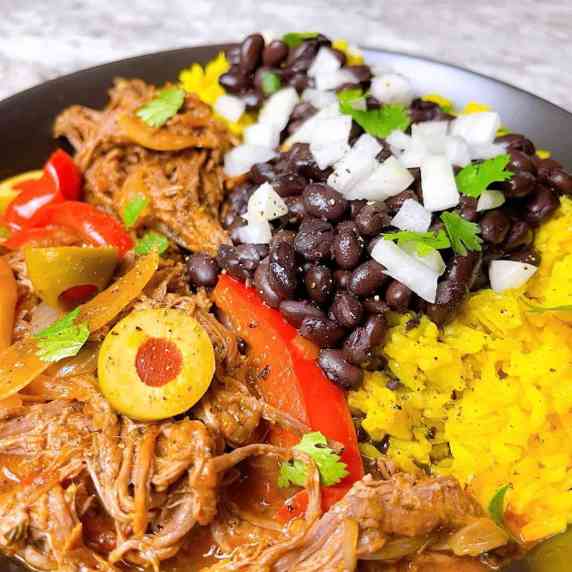 Close up of Ropa Vieja with yellow rice and black beans in black bowl