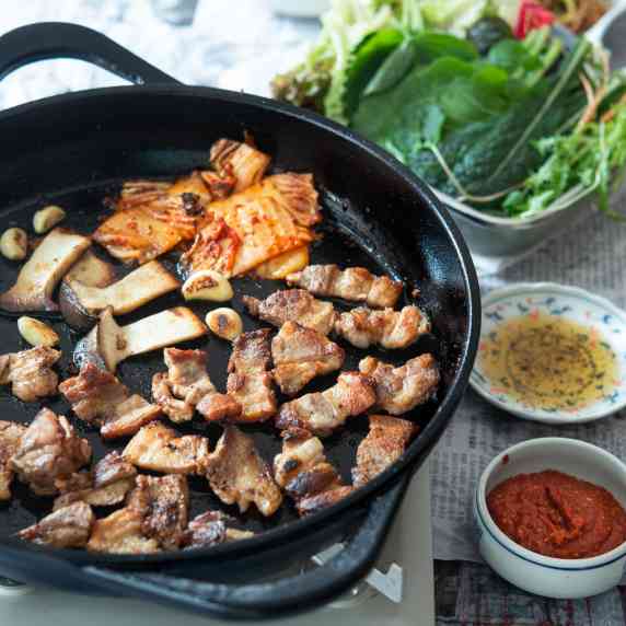 Korean pork belly and kimchi are grilled in a skillet and presented with toppings.