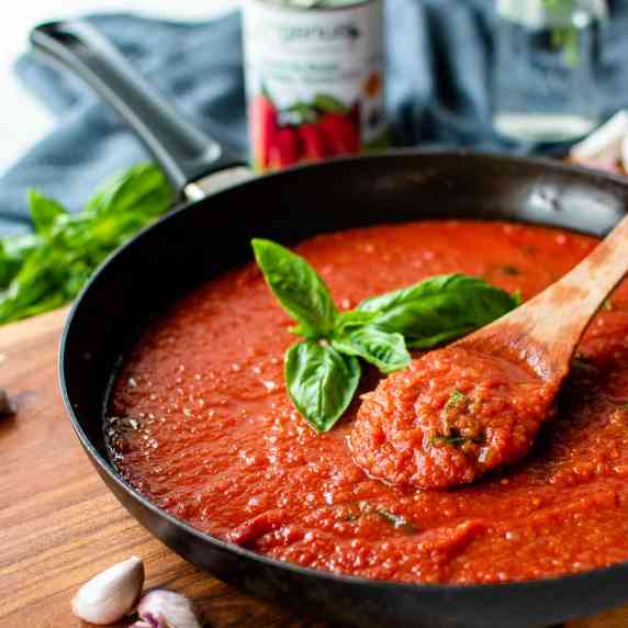tomato sauce in a black skillet with wooden spoon in the sauce and sprig of basil in the centre.