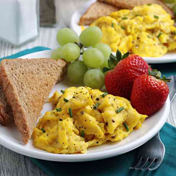 Scrambled eggs with toast and fruit on a white plate.
