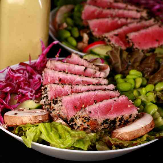 Two bowls of seared tuna salad with a bottle of wasabi vinaigrette.