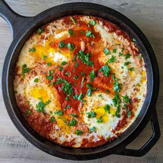 A cast iron skillet of shakshuka with eggs and cilantro