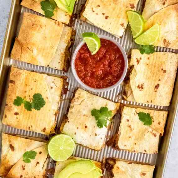 Overhead of ground beef sheet pan quesadillas cut into squares, served with salsa, avocado, and lime