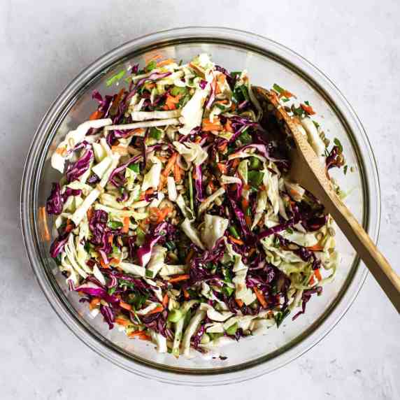 Healthy coleslaw in clear glass bowl with wooden spoon on light gray surface
