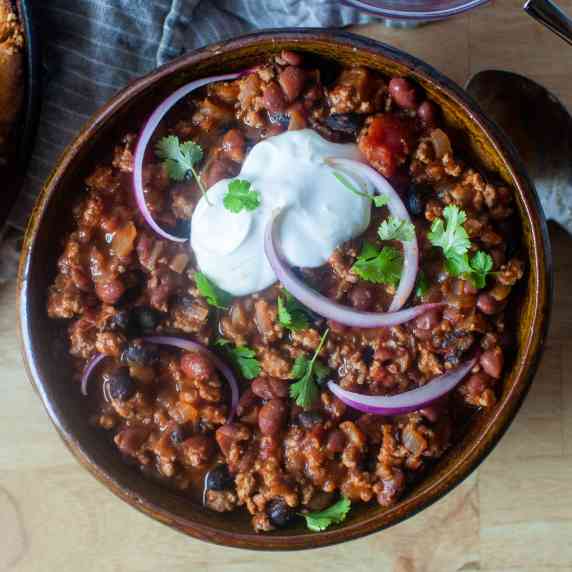 a bowl of turkey chili with sour cream and red onion on top