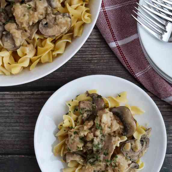 A plate of pasta with mushrooms next to the larger pan with a plate of many forks