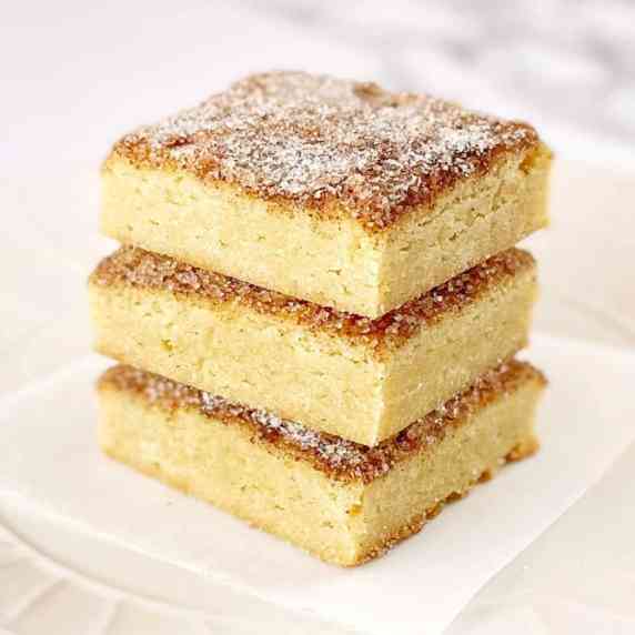 square pieces of snickerdoodle bars stacked up on a white plate.