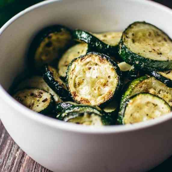 A white bowl filled with seasoned zucchini rounds.