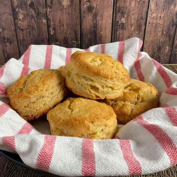 Biscuits stacked on a red & white striped towel nestled in a bowl.