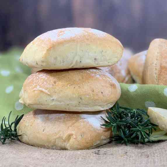 Sourdough Herb Ciabatta Rolls stacked next to rosemary with rolls on a green spotted towel behind.