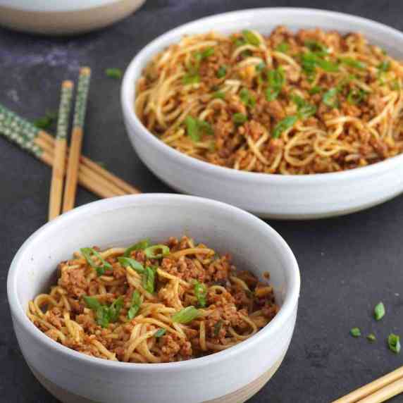 Two bowls of spicy noodles with chopsticks in the background.