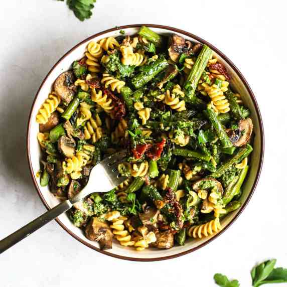 Pesto pasta with spring roasted veggies in beige bowl with fork