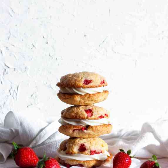A stack of three strawberry cheesecake cookies next to strawberries.
