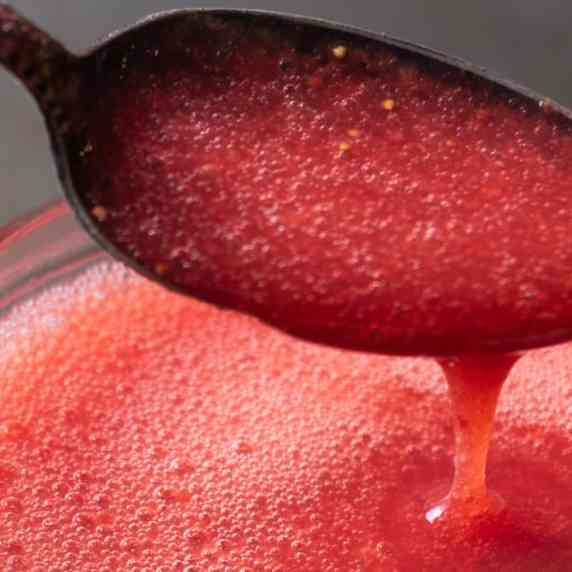 A spoon pouring strawberry puree into a jar.