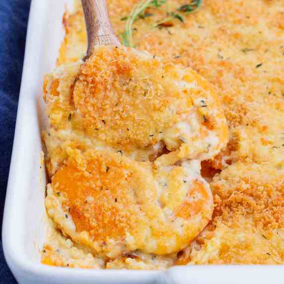Sweet Potatoes au Gratin RECIPE served in a white casserole dish with a wooden spoon.