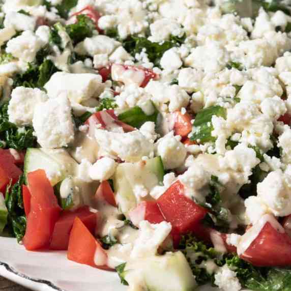 A platter of massaged kale salad with creamy tahini dressing, tomatoes, cucumbers, and feta.