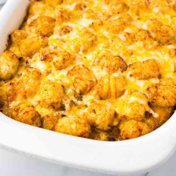 A casserole dish filled with a cheesy tater tot breakfast casserole at an angle.