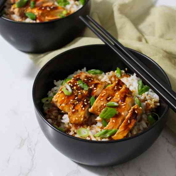 Teriyaki chicken with sesame seeds and scallions served over rice in a bowl with chopsticks