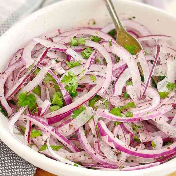 sliced red onions with parsley in a white bowl