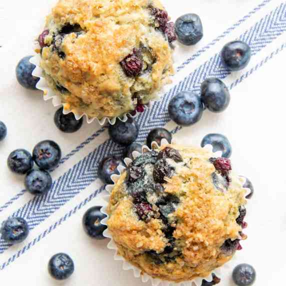 Overhead of two blueberry muffins with fresh blueberries all around them.
