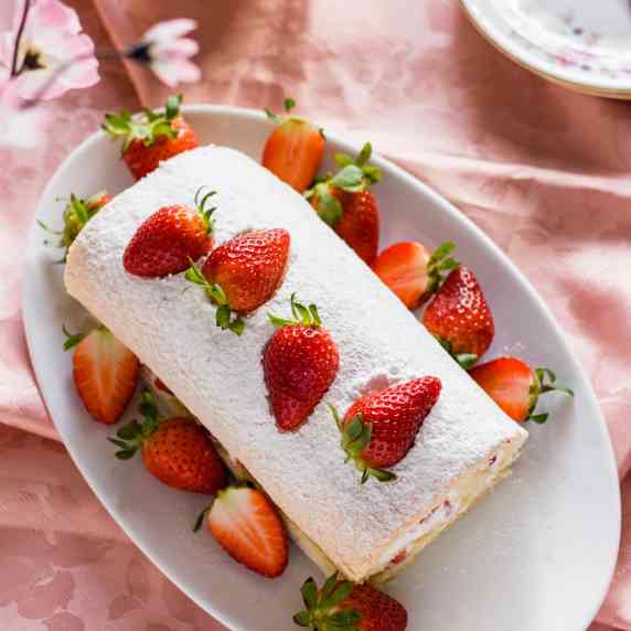 vanilla swiss roll cake on a white platter with strawberries
