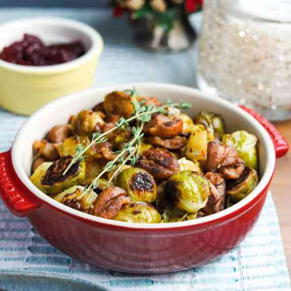 Photo of a red bowl filled with roasted sprouts and chestnuts and garnished with sprigs of thyme.