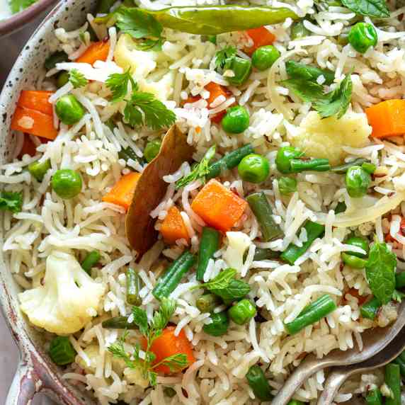 vegetable pulao served in a big serving bowl with two serving spoons
