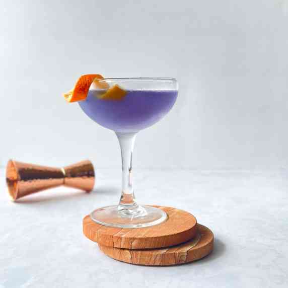 purple cocktail in a coupe with orange garnish and jigger.