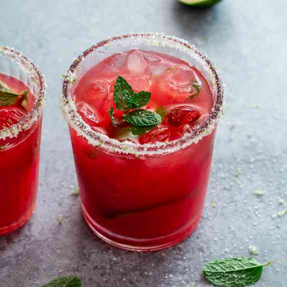  a round clear glass is filled with watermelon drink. the rim is covered with sugar
