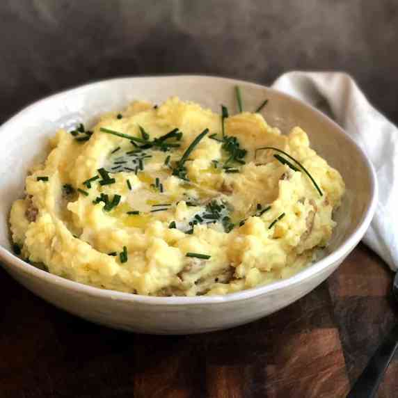 mashed potatoes in bowl with melted butter and chives on top