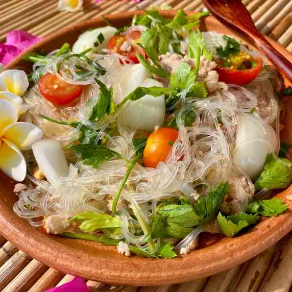 Yum woon sen (glass noodle salad) in a clay dish with tomatoes, celery, and onions.