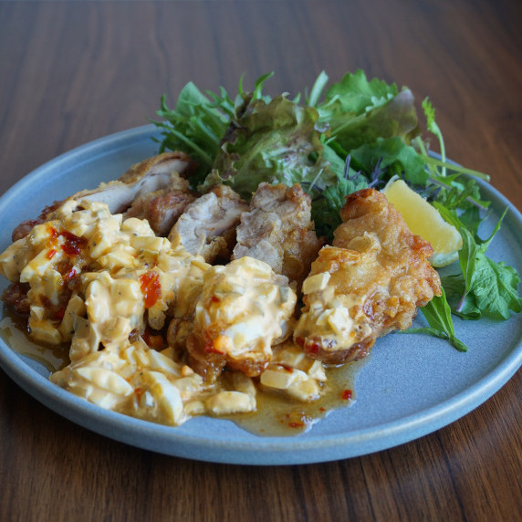 A dish of crispy fried chicken topped with tartar sauce and sweet chili sauce. 