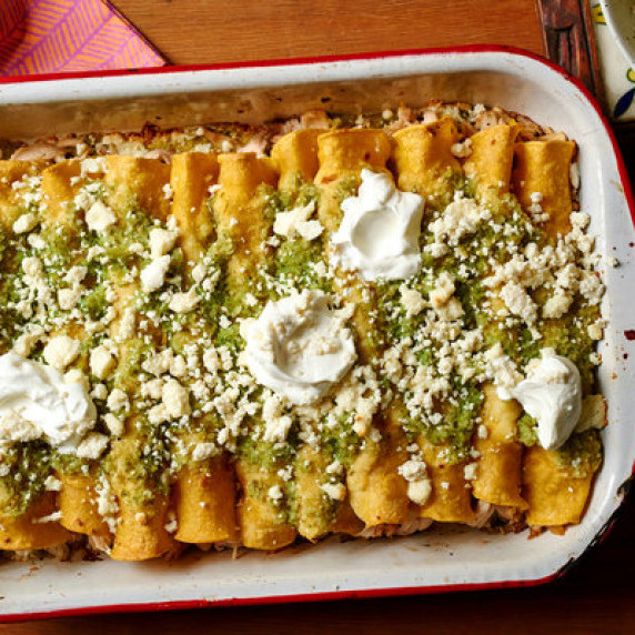 Enchiladas in baking dish topped with green salsa verde, Mexican crema, and queso fresco 