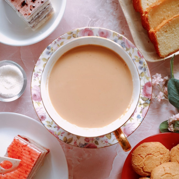 Japanese royal milk tea in a teacup surrounded by cookies and cake slices.