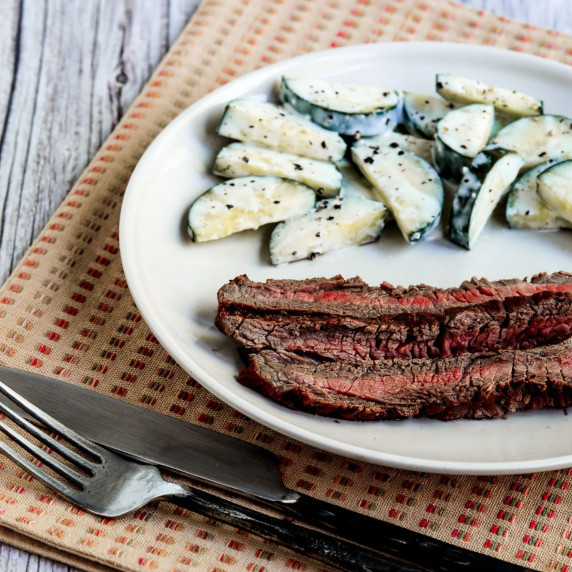 Marinated Grilled Flank Steak shown on serving plate with cucumber salad in background.