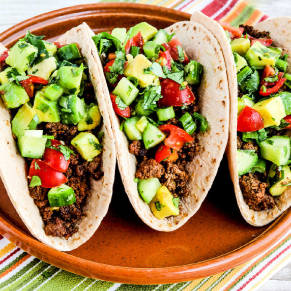 Three ground beef tacos with tomato avocado salsa shown on serving plate.