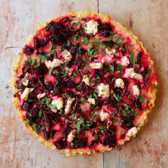 Overhead view of beet and feta tart with herbs on a wooden table.