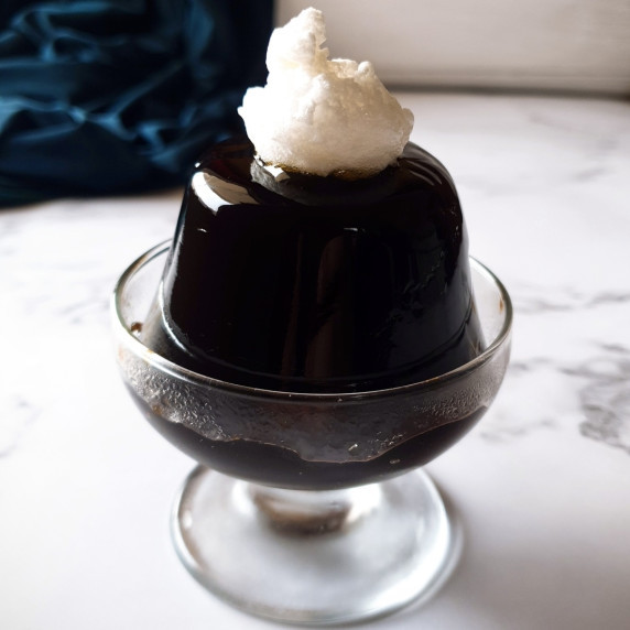 Coffee jello recipe in a small glass, topped with some sweet whipped cream.