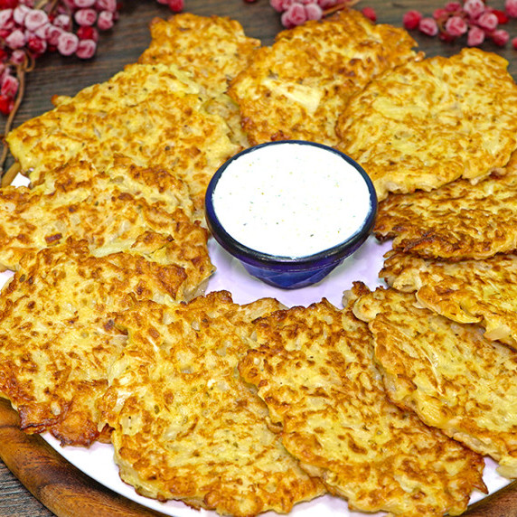 Cabbage fritters on a plate and a dipping sauce in the mddle.