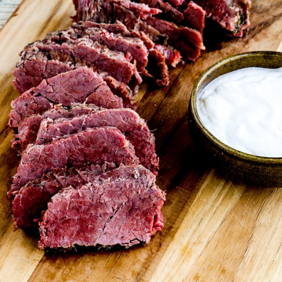 Instant Pot Corned Beef with Creamy Horseradish Sauce shown on cutting board with sauce in a bowl.