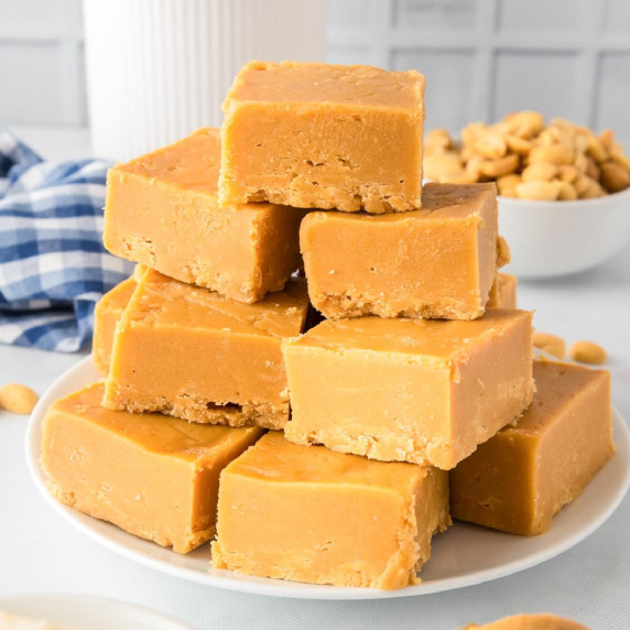 A stack of 2 ingredient peanut butter fudge squares on a plate stacked high from the side.